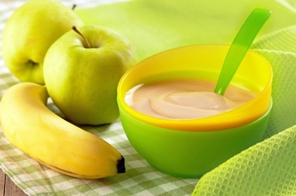 A bowl of baby food sitting on a table with an apple and a banana