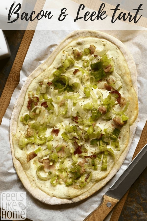 A pizza sitting on top of a wooden cutting board, with Tart and Bacon and Leek