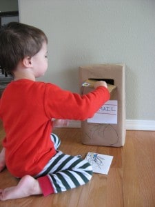 a little boy putting mail into a pretend mailbox