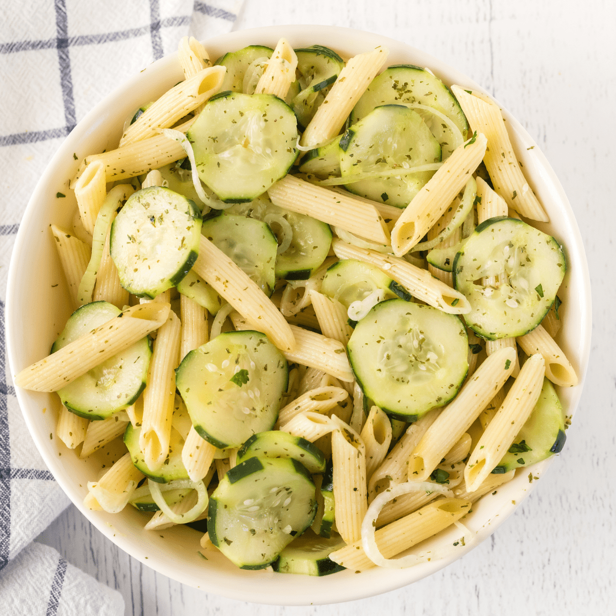 a white bowl filled with cucumbers, onions, and penne pasta