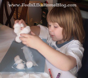 a little girl gluing cotton balls on a piece of blue paper