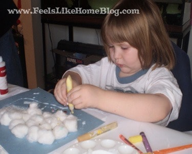 a little girl squeezing glitter glue on a piece of blue paper