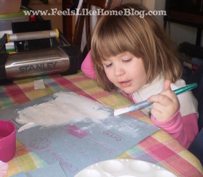 a little girl painting clouds on a piece of blue paper