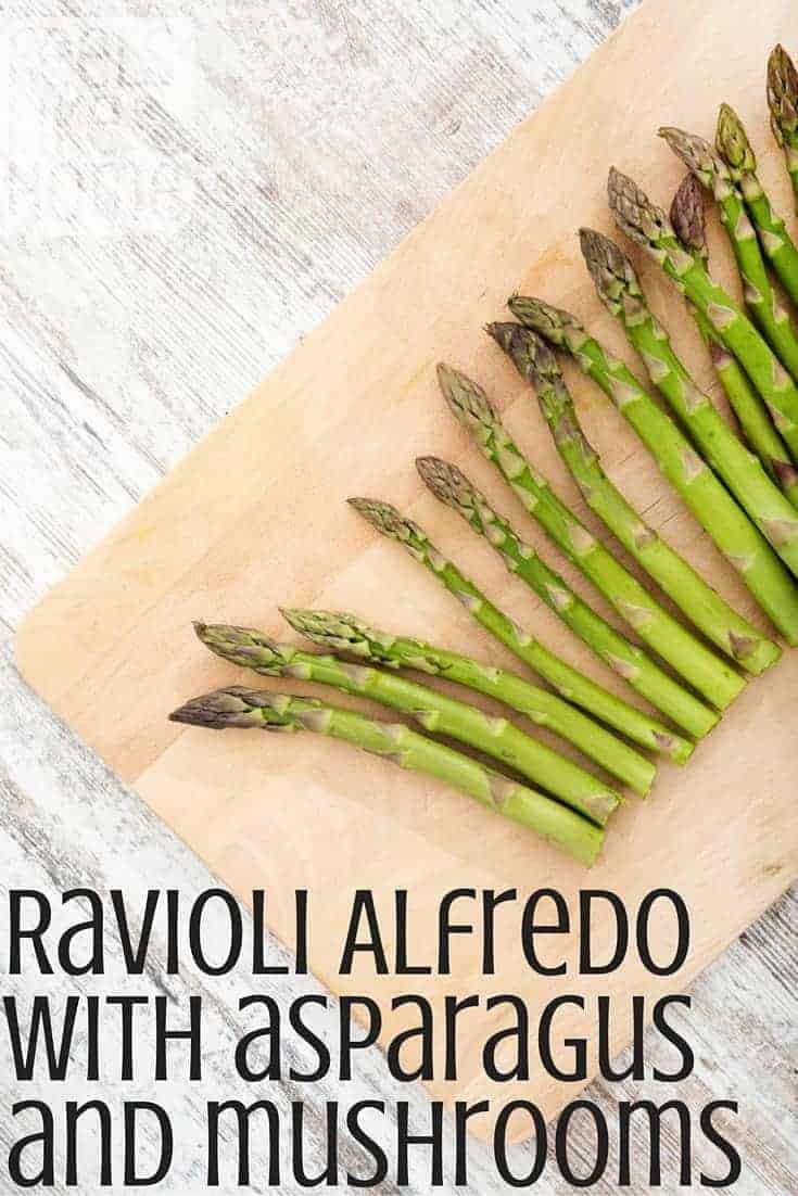 asparagus on a wooden cutting board with the title "ravioli alfredo with asparagus and mushrooms"