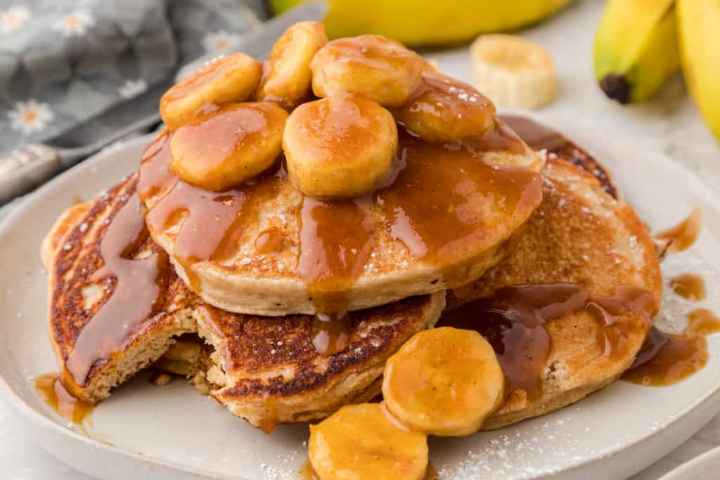 bananas foster pancakes on a plate with one bite missing