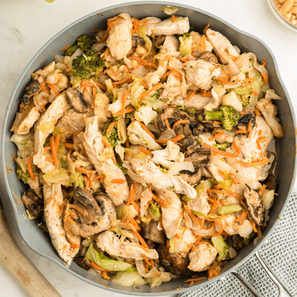 chicken and veggies in a skillet with peanut stir fry sauce