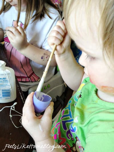 A little girl who is painting her eggshells with glue