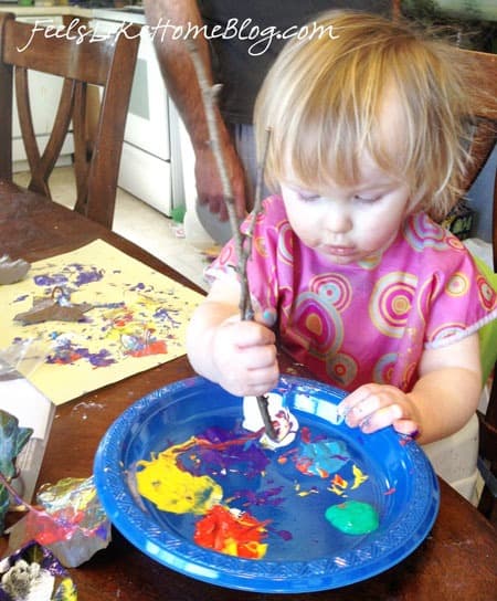 A little girl using a stick as a paint brush