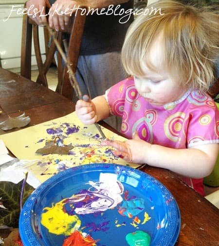 A little girl sitting at a table with a stick and paint