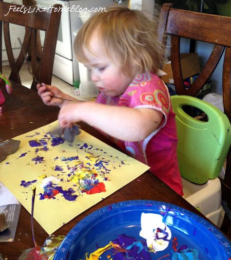A little girl using a leaf as a stamp in paint