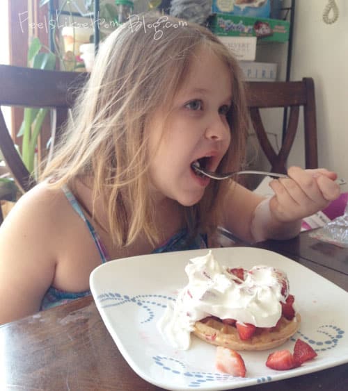 A little girl sitting at a table eating food, with Strawberry and Waffle