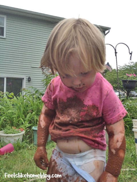 A muddy little girl that is sitting in the grass