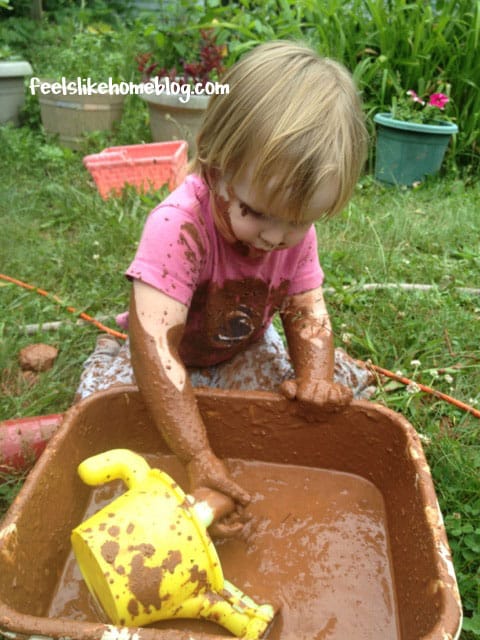 A little girl filling a watering can with mud