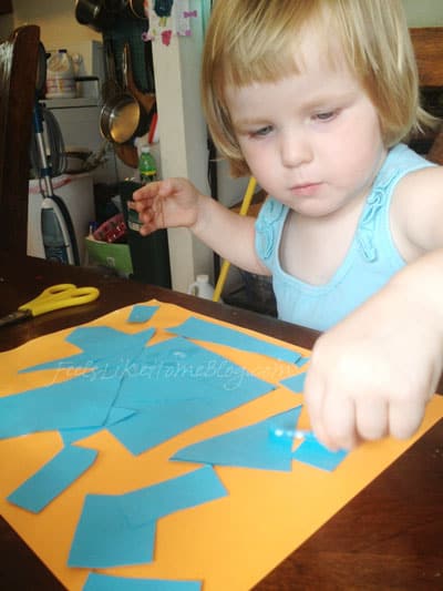 A little girl gluing a blue collage onto orange paper