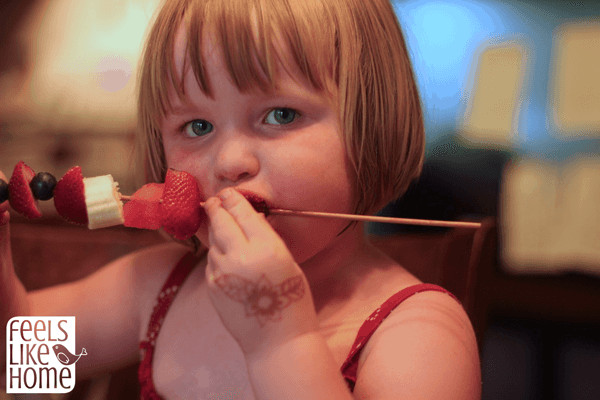 A little girl that is eating a fruit kabob