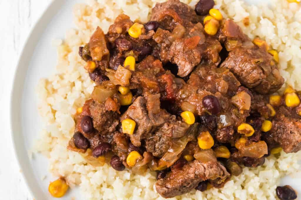 a close up of steak, corn, beans, and rice on a plate