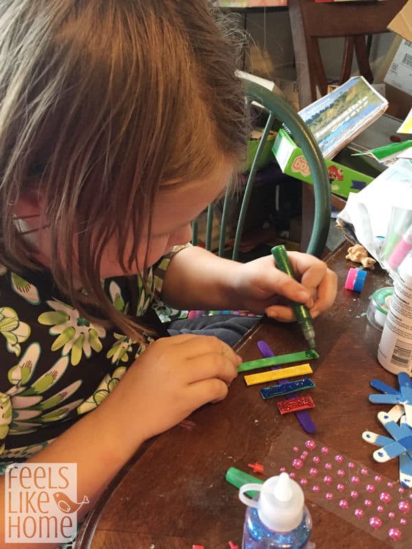 a little girl painting popsicle sticks with glitter glue