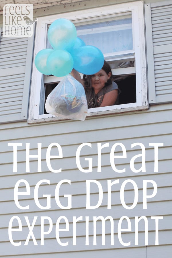 A kid hanging out a window with an egg drop experiment