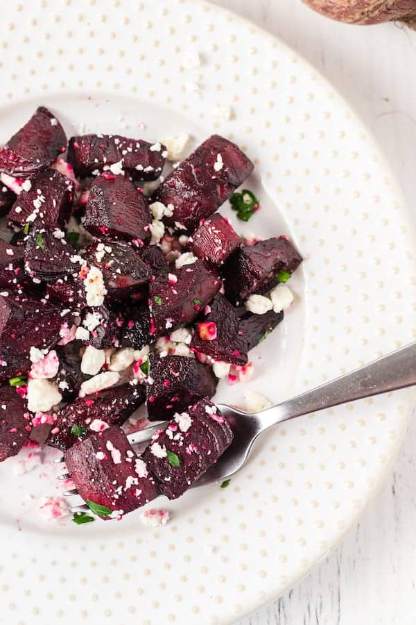 a pile of roasted red beets with feta cheese on a white plate with a fork