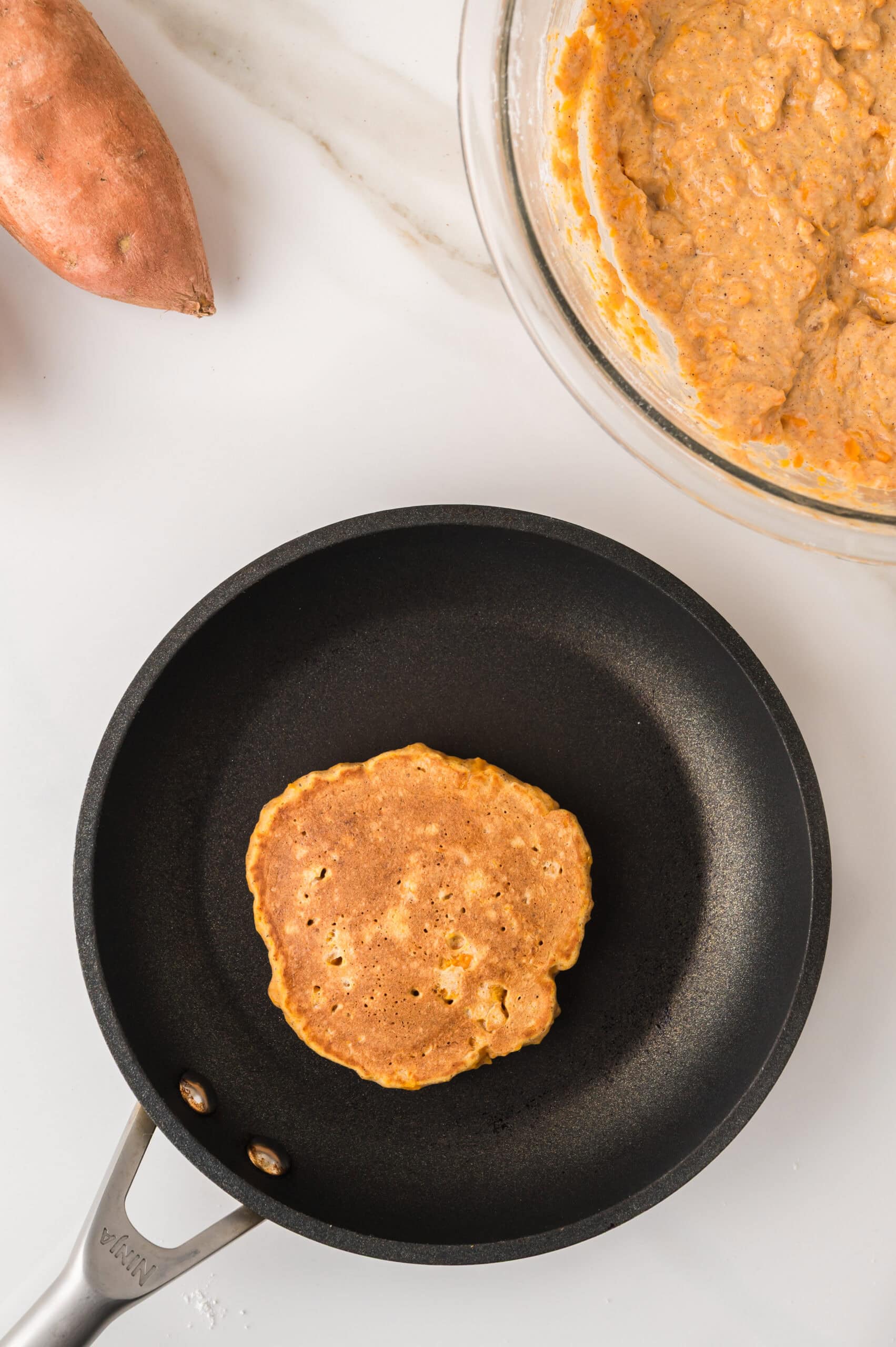 Golden sweet potato pancakes on griddle