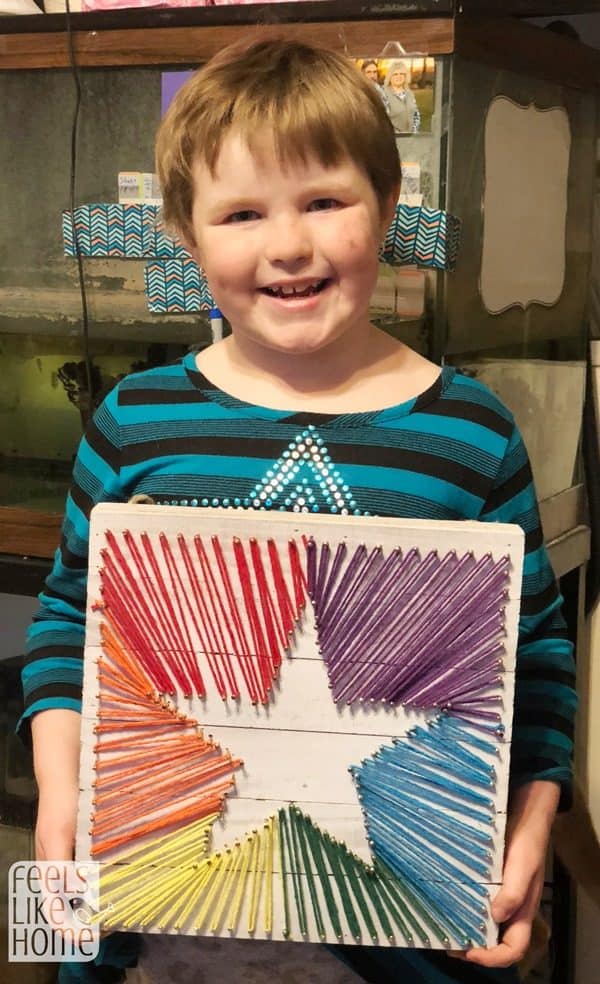 a young child holding her string art project