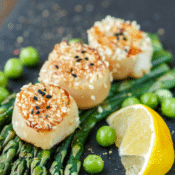 three seared scallops on top of asparagus spears with a wedge of lemon