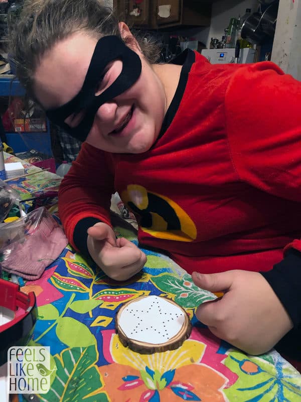 A tween girl in a superhero costume working on string art