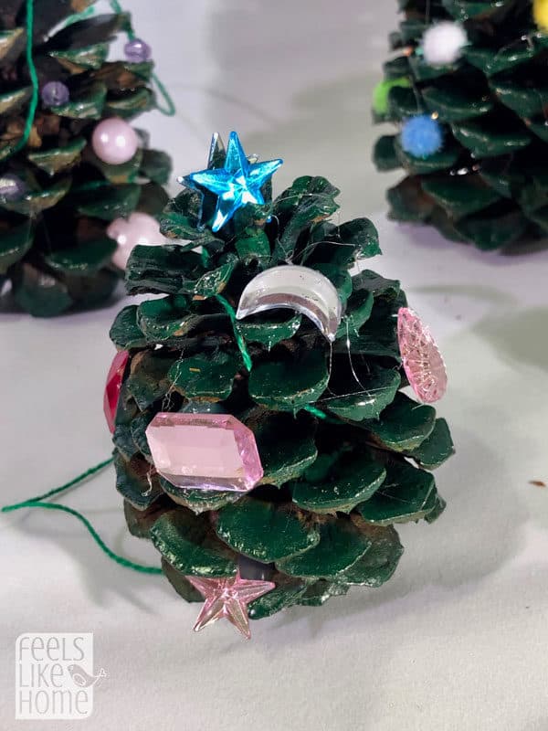 A close up of a pine cone Christmas tree with jewels for ornaments