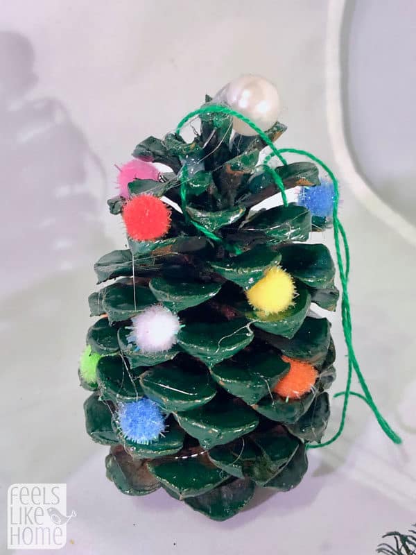 A close up of a pine cone Christmas tree with pompoms for ornaments