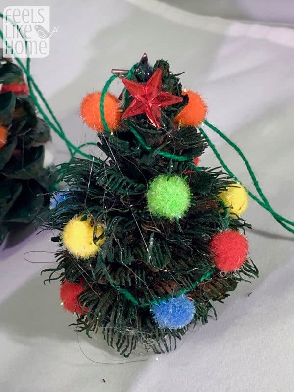 A close up of a pine cone Christmas tree with pompoms for ornaments