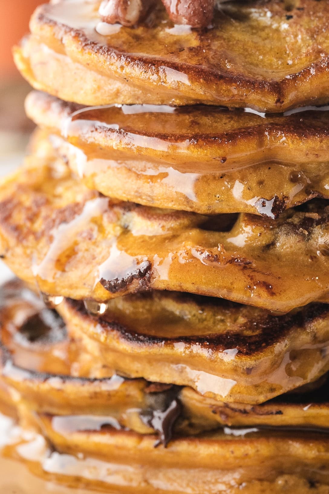 Pumpkin spice pancakes piled high, up close with maple syrup drizzling down