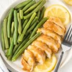 lemon chicken sliced on a white plate with green beans and lemon slices