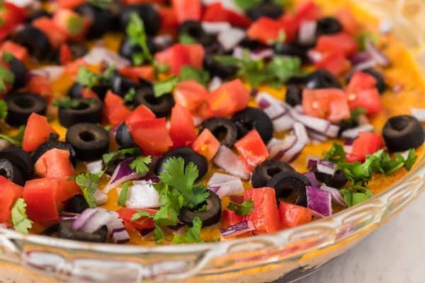 up close healthy taco dip with diced tomatoes, black olives, onion, and cilantro