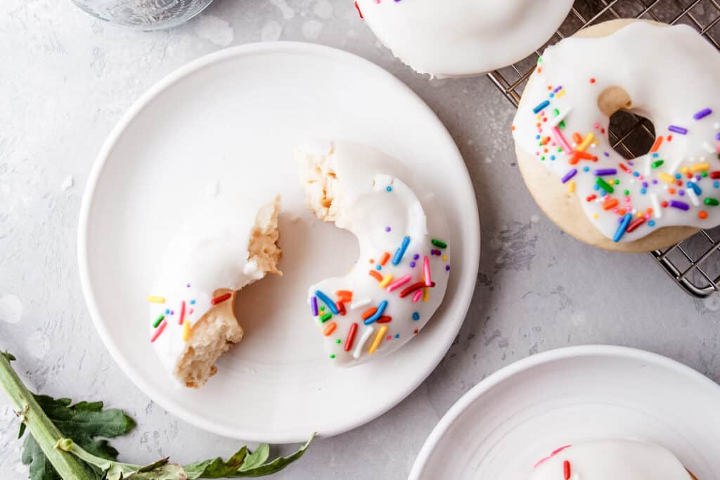 one baked vanilla cake donut with white frosting and colored sprinkles broken in half