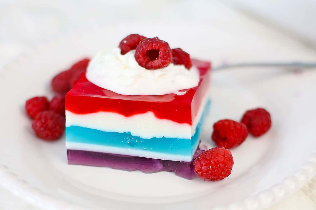 one square of layered jello on a plate with fresh raspberries