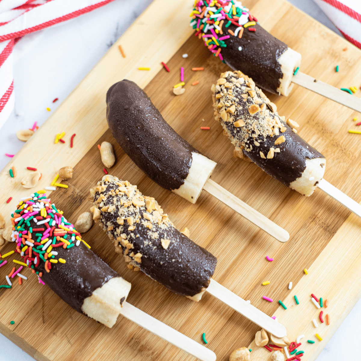 five chocolate covered banana pops on a wooden cutting board