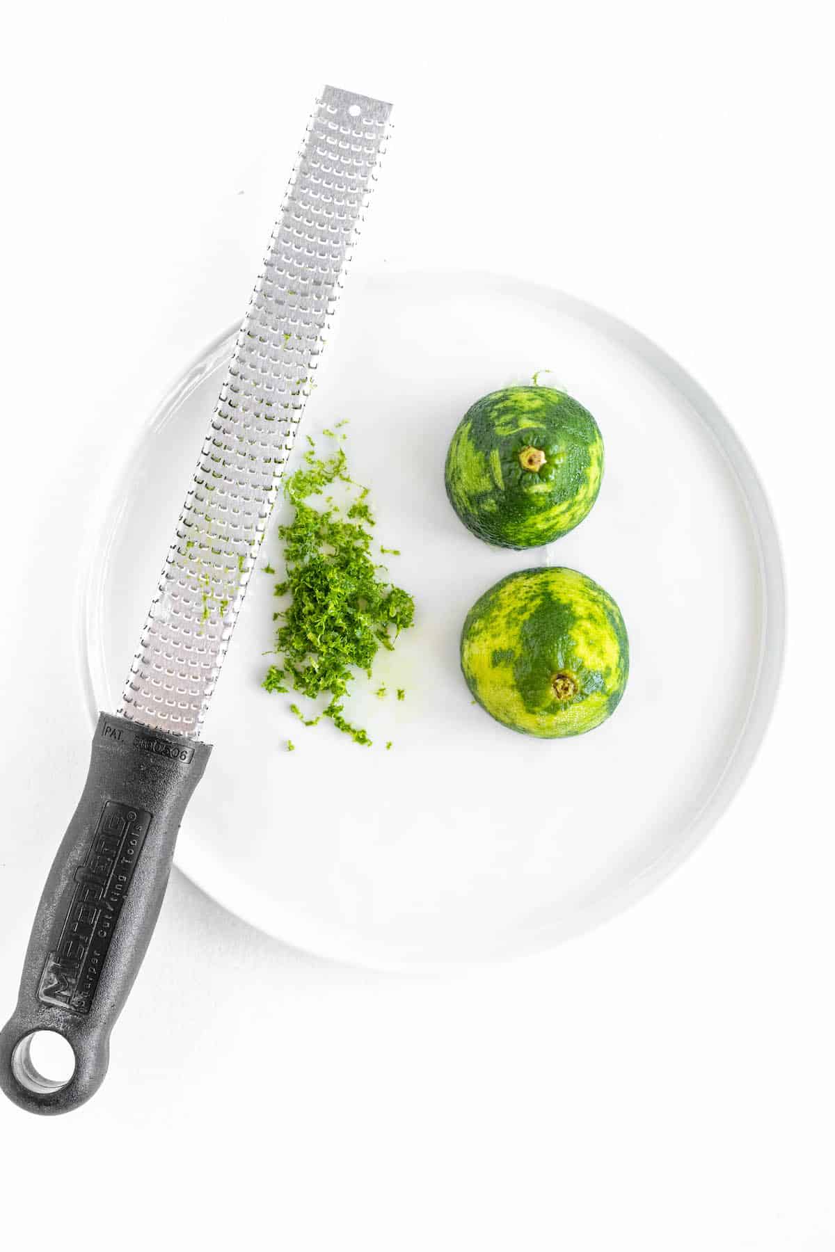 two lime halves with a microplane grater and a pile of lime zest