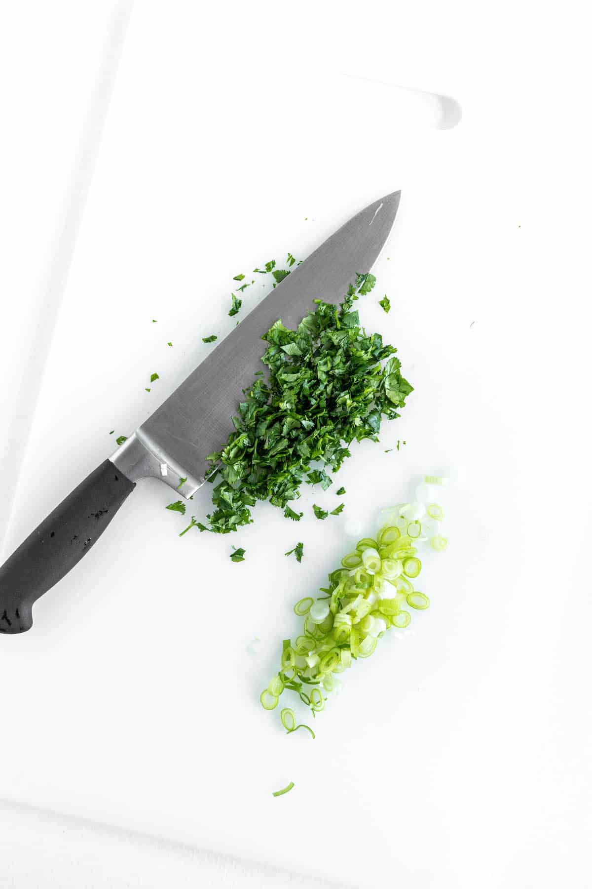 chopped cilantro with a large knife of a white cutting board