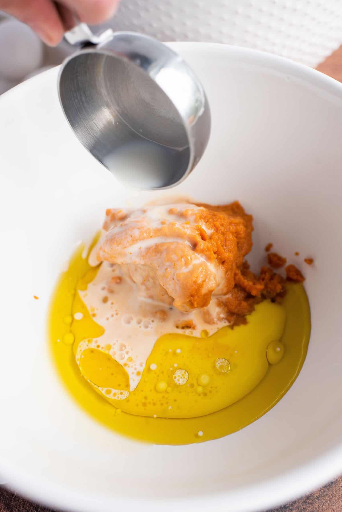 adding milk and oil to the pumpkin in the mixing bowl