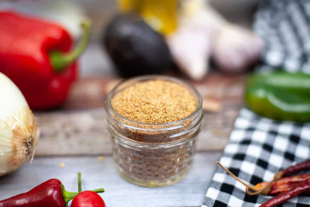 homemade fajita seasoning in a small jar with peppers, onions, and garlic around it