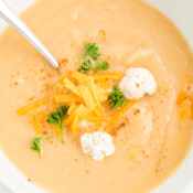 a close up of cheesy cauliflower soup topped with cheddar cheese and raw cauliflower