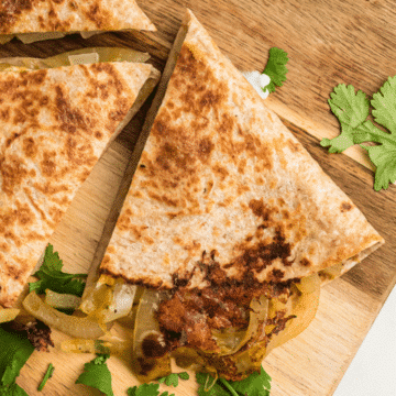 a close up of the best cheese and onion quesadillas on a wooden cutting board