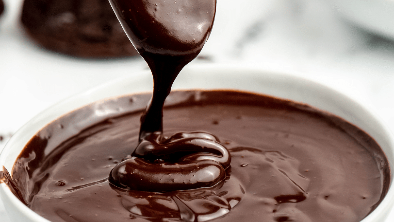 a close up of the best hot fudge dripping off of a spoon into a white bowl