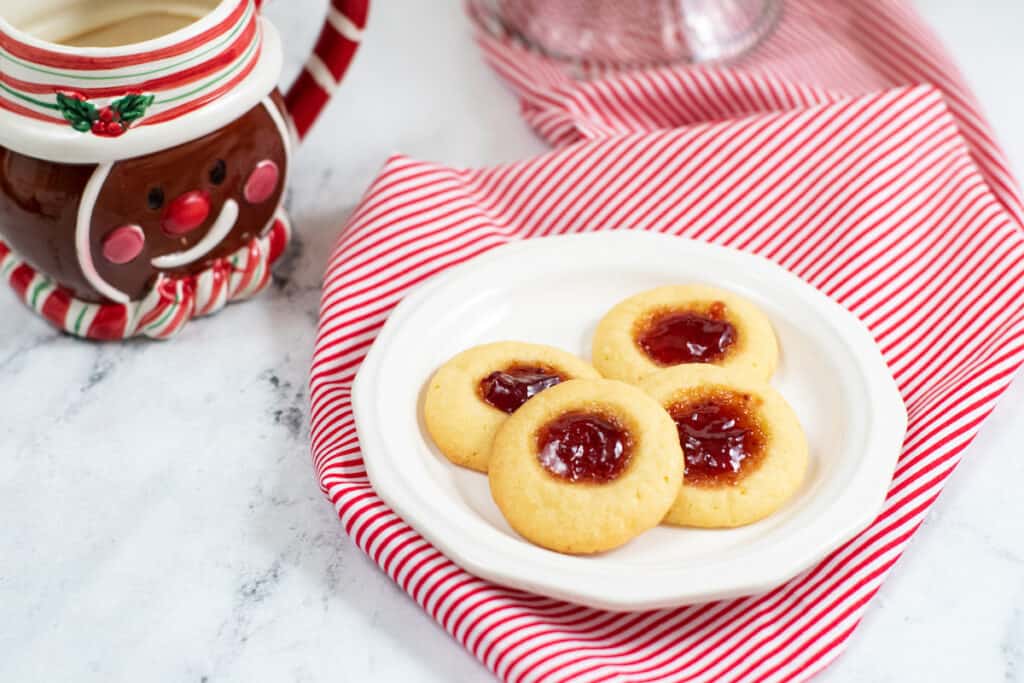 a plate with 4 thumbprint sugar cookies with jam centers on it and a gingerbread man mug in the background