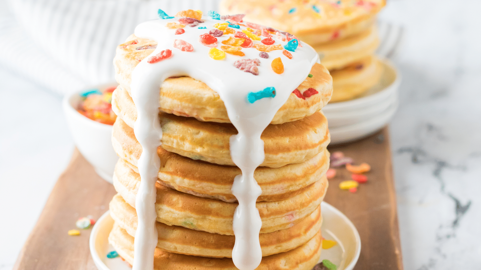 a stack of Fruity Pebbles pancakes topped with melted marshmallow fluff and Fruity Pebbles cereal