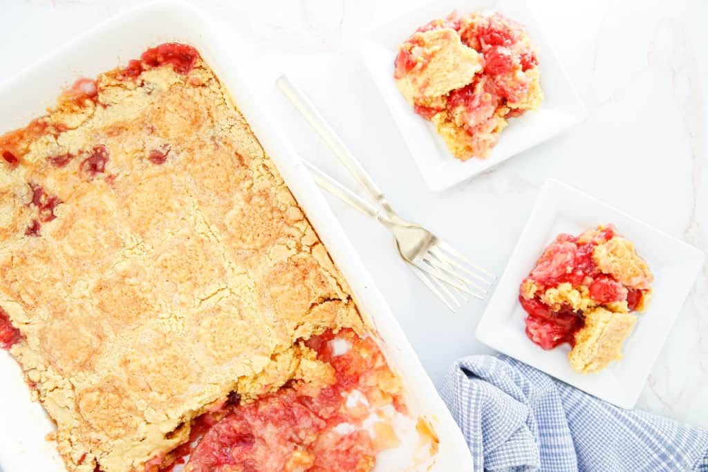 cherry pineapple dump cake in the baking dish with two individual servings on white plates