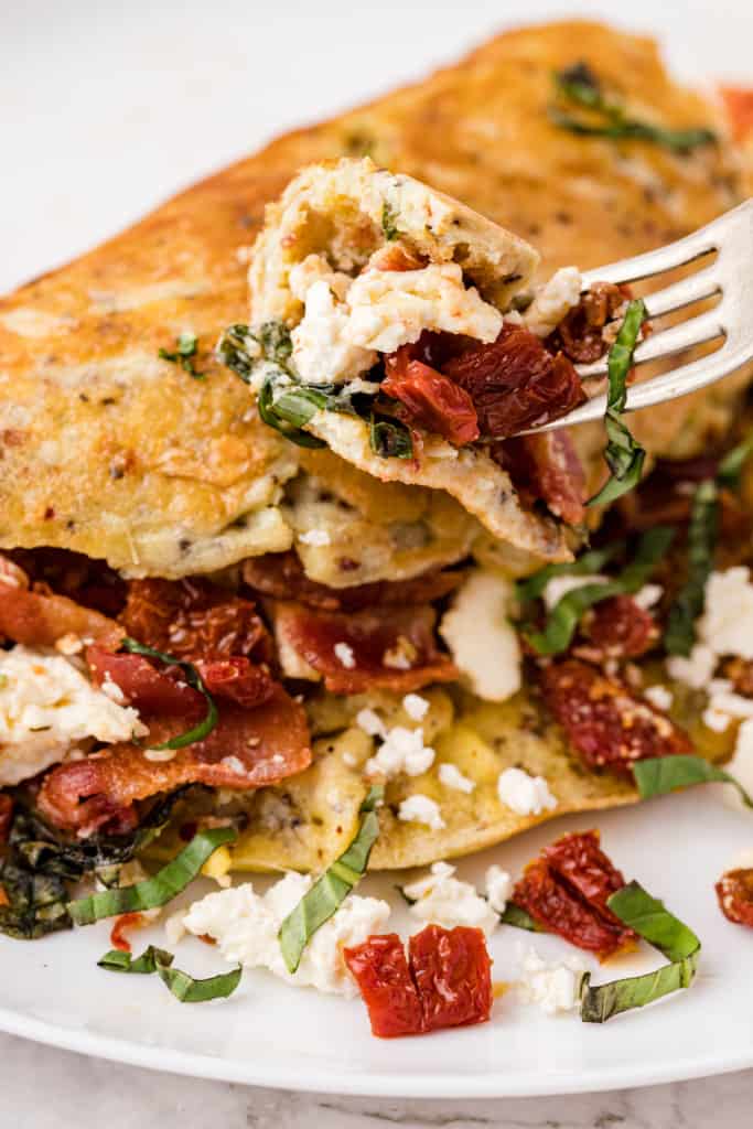 one bite of sun-dried tomato omelet with bacon and feta cheese