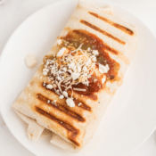 a grilled chicken burrito topped with salsa verde and queso blanco on a white plate