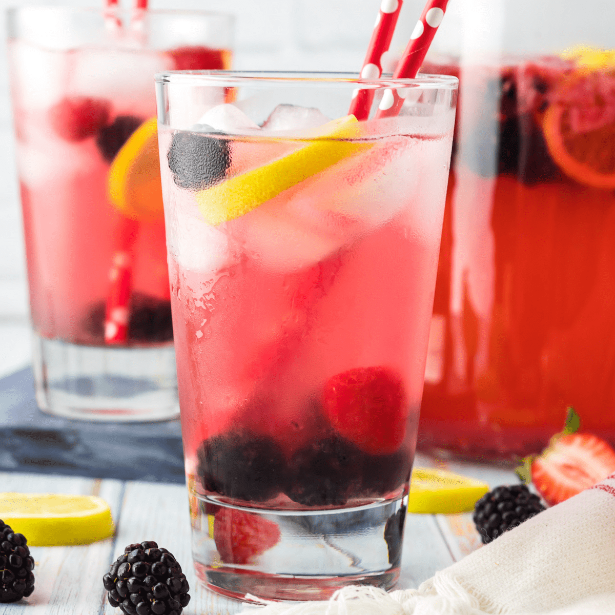 A glass of sparkling pink lemonade with berries with two red straws