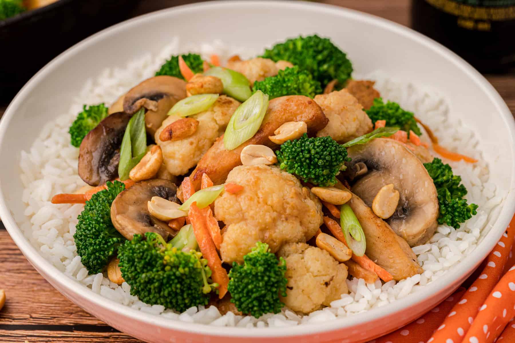 stir fry with chicken and broccoli, cauliflower, and carrots with a peanut stir fry sauce, served over rice on a white plate